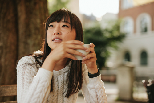 woman sitting on park bench while holding cup of coffee