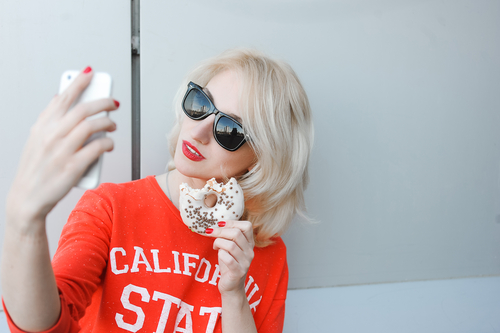 woman taking selfie while wearing black sunglasses and holding a donut